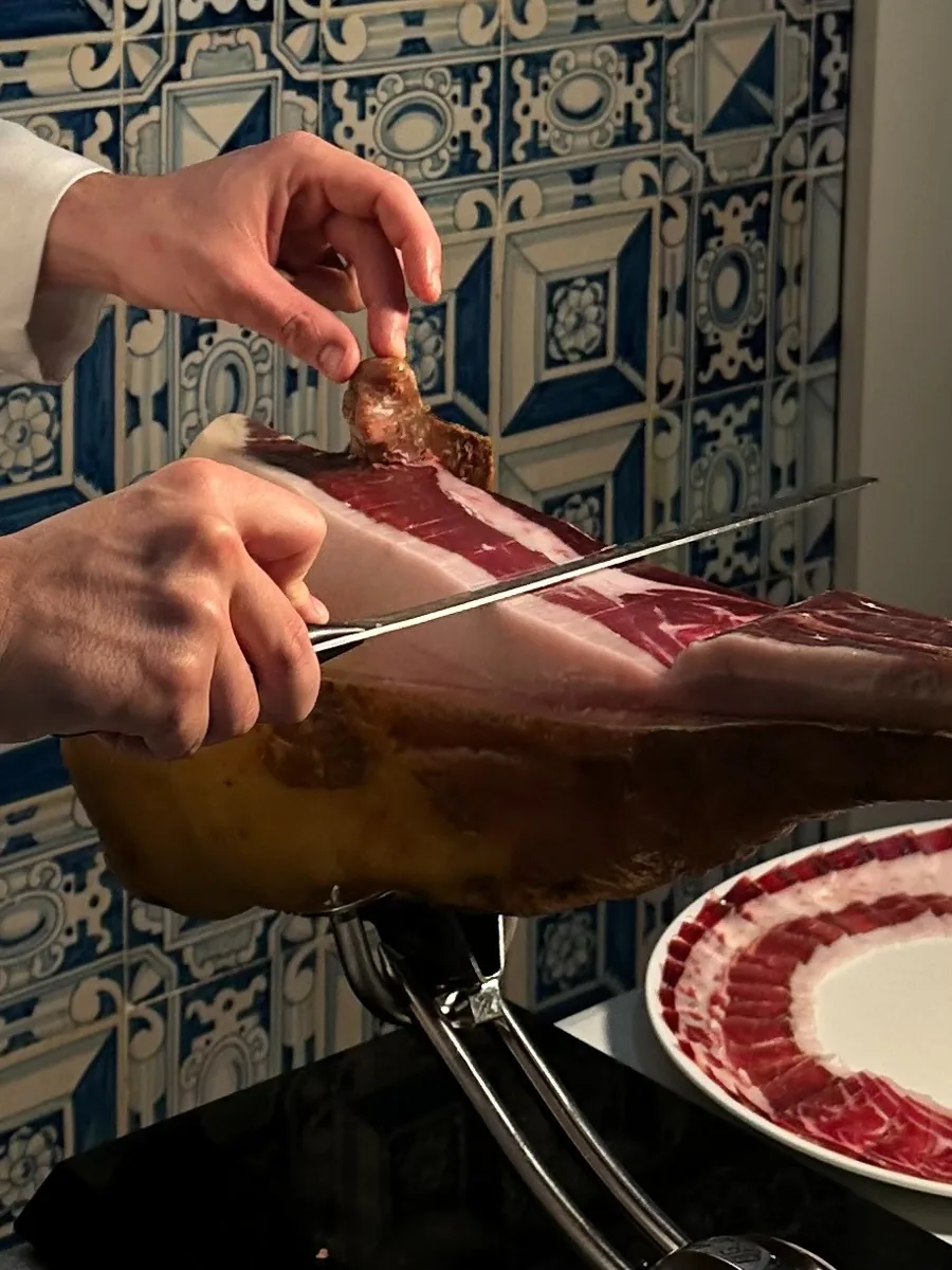 Manos cortando una loncha de jamón a cuchillo