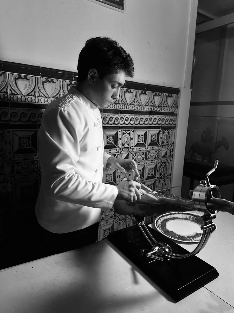 Cortador trabajando una pieza de jamón en blanco y negro